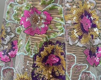 May include: Close-up of a delicate, light blue mesh fabric with intricate floral embroidery. The flowers are made of sequins in shades of pink, yellow, purple, and green.