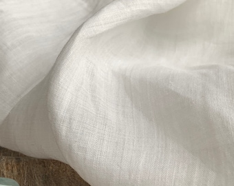 Puede incluir: Tela de lino blanco con una superficie suave y texturizada. La tela está drapeada sobre una superficie de madera.