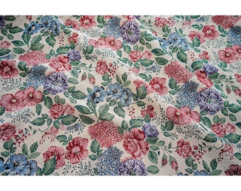 May include: A beige fabric with a floral pattern featuring pink, blue, and purple flowers. The fabric has a textured surface and a slightly wrinkled appearance.