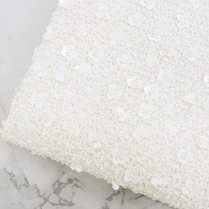 May include: White fabric with a textured weave and small white sequins throughout.