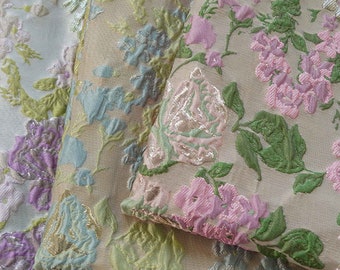 May include: Three pieces of fabric with floral patterns. The fabric is a brocade with a raised texture. The patterns are in shades of pink, blue, green, and silver.