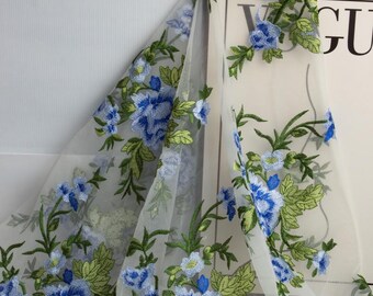 Puede incluir: Tela blanca transparente con un patrón floral bordado en azul y verde. La tela es delicada y tiene una textura suave y fluida.