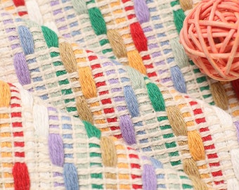 Puede incluir: Primer plano de una tela tejida con un patrón de rayas de colores. La tela está hecha de fibras naturales y tiene un tacto suave y texturizado. Los colores son brillantes y vibrantes, incluyendo rojo, naranja, amarillo, verde, azul y morado.