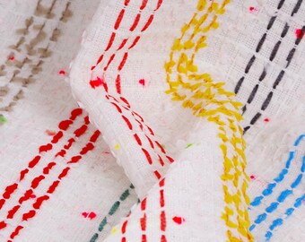 Puede incluir: Tela blanca con rayas de colores rojo, amarillo, azul y verde. Las rayas están hechas de líneas cosidas.