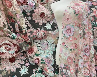 May include: Floral embroidered fabric with pink, white, and teal sequins. The fabric features large flower designs and smaller floral accents. The fabric is draped over a mannequin, showcasing the intricate details and texture.