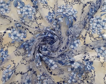 Puede incluir: Bordado floral azul sobre una tela blanca transparente. La tela es delicada y tiene una textura suave y fluida.