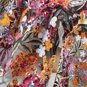 Könnte beinhalten: Schwarzer Netzstoff mit gestickten Blumenmustern in Rosa-, Orange- und Weißtönen. Der Stoff ist mit Pailletten besetzt.