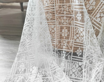 May include: White lace fabric with a geometric pattern. The fabric is sheer and delicate, with a soft, flowing texture.