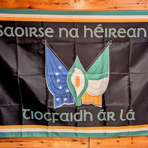 May include: Black flag with the text "Saoirse na hÉireann" and "Tiocfaidh ár Lá" in white. The flag features three stylized flags in blue, green, and white, with a central floral emblem. The flag has a green, white, and orange border.