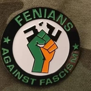 Può includere: Uno spillo circolare bianco e nero con il testo "FENIANS AGAINST FASCISM" in lettere verdi attorno al bordo. Un pugno verde e arancione è al centro del cerchio.