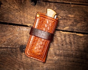 May include: A brown leather knife sheath with a woven pattern and a brown leather strap. The sheath is designed to hold a pocket knife.