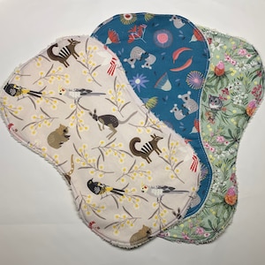 May include: Three cloth pads with unique patterns. One is beige with Australian animals and yellow flowers. Another is teal with koalas and floral designs. The third is green with pink flowers and small animals.