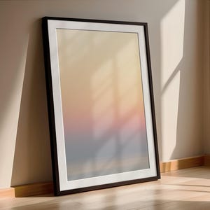 Könnte beinhalten: Ein gerahmter Kunstdruck mit einem weichen Farbverlauf aus Gelb, Rosa und Blau. Das Kunstwerk wird in einem schwarzen Rahmen mit weißem Passepartout präsentiert und lehnt an einer neutralfarbenen Wand. Der Druck befindet sich auf einem Holzboden.