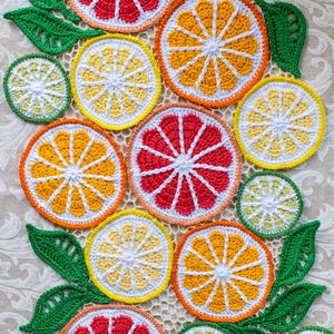 Puede incluir: Colección de coloridas rodajas de frutas cítricas tejidas a ganchillo, incluyendo naranjas, limones, limas y pomelos. Los posavasos hechos a mano presentan centros blancos y están rodeados de hilo naranja, amarillo, rojo y verde. Hojas verdes tejidas a ganchillo se intercalan entre la fruta.