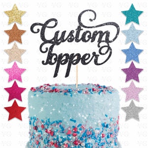K&ouml;nnte beinhalten: Schwarzer Glitzer-Kuchentopper mit dem Text "Custom Topper" auf einem blau glasierten Kuchen mit bunten Streuseln. Der Topper ist auf einem Stiel und bereit, auf einen Kuchen gelegt zu werden.