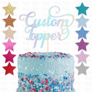 K&ouml;nnte beinhalten: Ein Kuchentopper mit den Worten "Custom Topper" in schimmernden Buchstaben. Der Topper befindet sich auf einem blauen Kuchen mit rosa und blauen Streuseln. Im Hintergrund befinden sich 10 glitzernde Sterne in verschiedenen Farben.