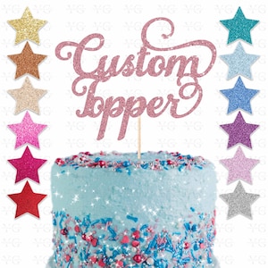 K&ouml;nnte beinhalten: Rosa glitzernder Tortendekor mit den Worten "Custom Topper" auf einem blau gefrosteten Kuchen mit Streuseln. Der Tortendekor ist auf einem Holzstiel.