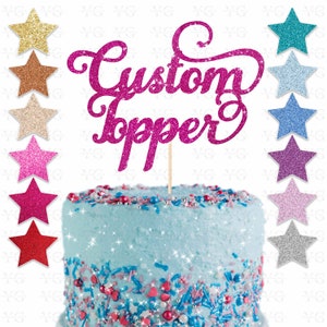 K&ouml;nnte beinhalten: Ein rosa glitzernder Tortendekor mit den Worten "Custom Topper" in einer kursivschrift. Der Dekor befindet sich auf einem blau gefrosteten Kuchen mit bunten Streuseln.