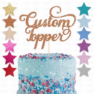 K&ouml;nnte beinhalten: Ein goldener Glitzer-Kuchentopper mit den Worten "Custom Topper" in einer kursiv geschriebenen Schrift. Der Topper befindet sich auf einem blau gefrosteten Kuchen mit bunten Streuseln. Das Bild zeigt auch eine Vielzahl von Glitzersternen in verschiedenen Farben.