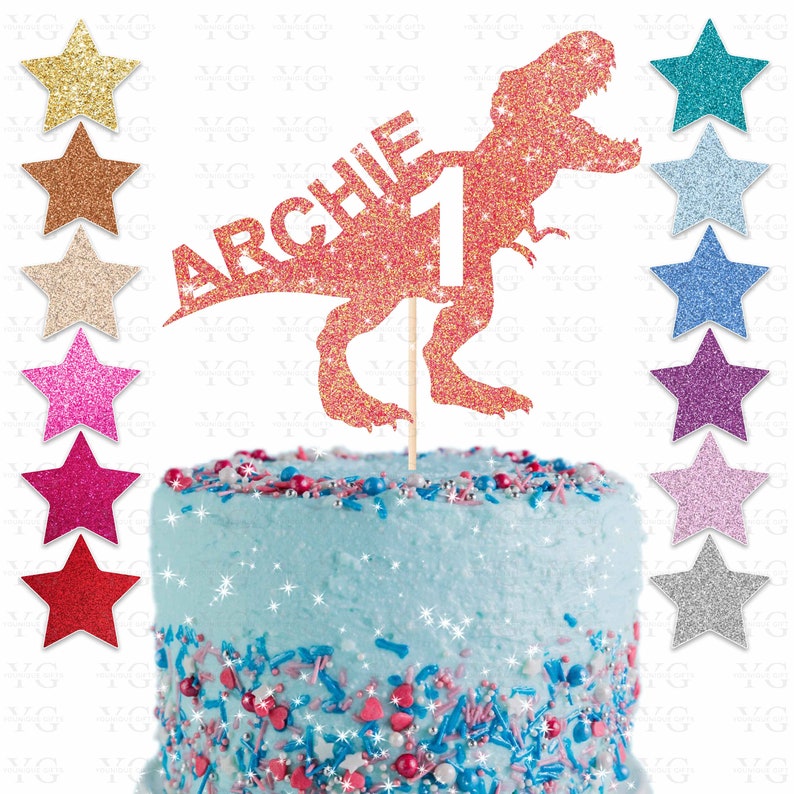 May include: A glittery orange Tyrannosaurus Rex cake topper with the name "ARCHIE" and the number "1". The cake is light blue with colorful sprinkles. Various glitter star decorations are arranged around the cake.
