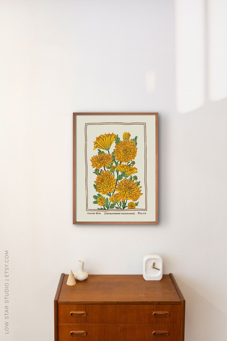 May include: A framed botanical print featuring yellow chrysanthemum flowers with green leaves on a cream background, enclosed in a brown border. The text at the bottom reads Garden Mum (Chrysanthemum grandiflorum) Fig. 016 in a dark brown font.