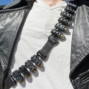 Könnte beinhalten: Eine schwarze Lederjacke mit einem schwarzen und silbernen Patronengurt, der über einem weißen T-Shirt getragen wird.