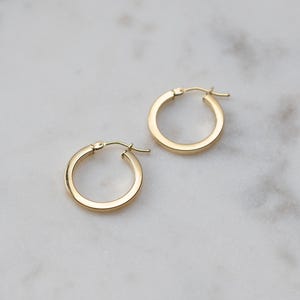 May include: A pair of small, polished gold hoop earrings with a smooth, rounded surface and a hinged post closure. The earrings feature a simple, circular design with a reflective metallic finish, showcasing a classic and clean aesthetic.