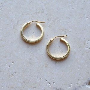 May include: A pair of polished gold hoop earrings with a smooth, rounded profile and a hinged post closure. The earrings feature a classic circular design with a reflective metallic finish, showcasing a simple and clean aesthetic for everyday wear.