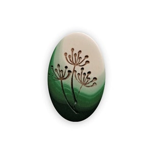 Könnte beinhalten: Eine ovale Keramikfliese in Weiß und Grün mit einer braunen Silhouette von drei stilisierten Blumen.