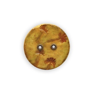 Könnte beinhalten: Ein runder, gelber Knopf mit zwei Löchern und einem Design aus stilisierten Löwenzahnpflanzen.