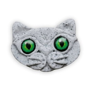 Könnte beinhalten: Eine graue Katzenfigur mit grünen Augen. Die Katze hat eine strukturierte Oberfläche und einen verspielten Ausdruck.