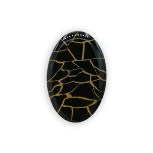 Könnte beinhalten: Schwarzer ovaler Harz-Cabochon mit goldenem Craquelé-Muster.