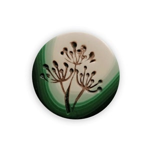 Könnte beinhalten: Eine runde Keramikfliese mit einem grün-weißen Wirbelmuster. Eine braune Silhouette von drei Blütenzweigen ist mittig auf der Fliese platziert.