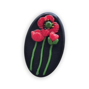 Könnte beinhalten: Eine schwarze, ovale Keramikfliese mit drei roten Mohnblumen mit grünen Stielen und Blättern.