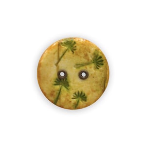 Könnte beinhalten: Ein runder, gelber Knopf mit grünem Blumenmuster und zwei Löchern.