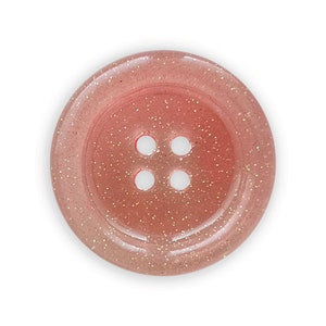 Könnte beinhalten: Ein rosa Knopf mit glitzernder Oberfläche und vier Löchern.