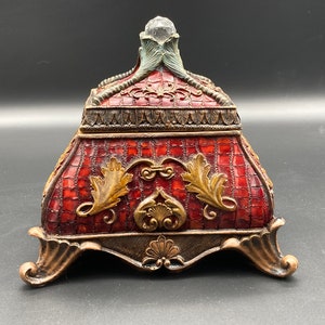 May include: A red and gold decorative box with a crystal top and ornate detailing. The box has a checkered pattern and intricate floral designs.