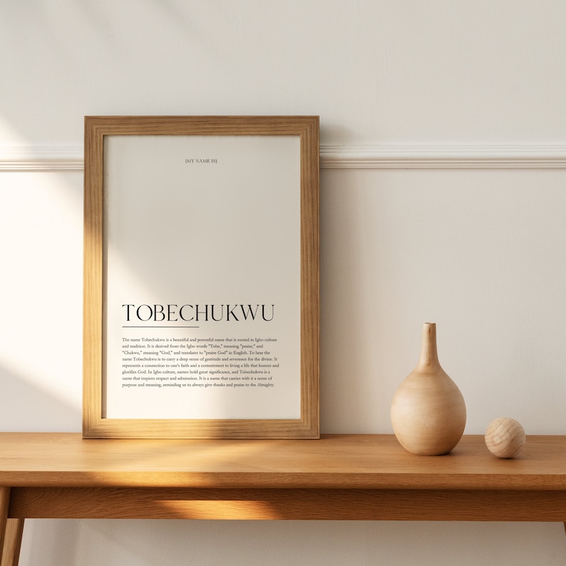 May include: A framed print with the name "TOBECHUKWU" in bold black text. The print explains the meaning of the name, which is a beautiful and powerful name that is meant to inspire calm and wisdom. The name is of Igbo origin and means "God is Great".