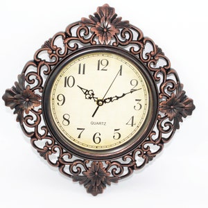 May include: A round, antique-style wall clock with a decorative, ornate frame. The clock face is cream-coloured with black Roman numeral markings and a quartz movement.