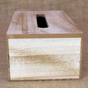 May include: A rectangular wooden tissue box cover featuring a natural light brown wood grain finish on the top surface and a contrasting white-washed wood grain finish on the front panel, with a centered elongated oval opening for dispensing.