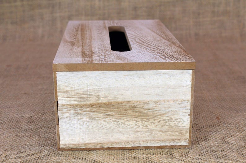 May include: A rectangular wooden tissue box cover featuring a natural light brown wood grain finish on the top surface and a contrasting white-washed wood grain finish on the front panel, with a centered elongated oval opening for dispensing.