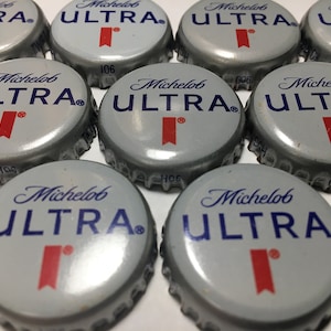 May include: Close-up of nine silver bottle caps with the Michelob ULTRA logo in blue and red. The caps are arranged in a semi-circle.