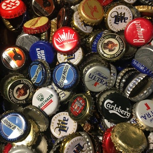 May include: A collection of colorful bottle caps with various brand names and logos, including Bud Light, Blue Moon, Michelob Ultra, and Carlsberg.