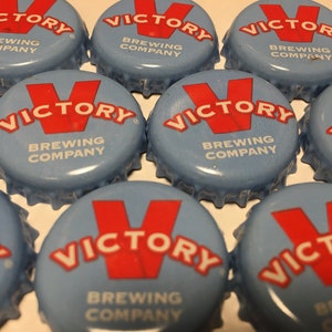 May include: Several light blue bottle caps, each featuring the text "VICTORY BREWING COMPANY" in red and white. The caps are arranged in a grid, highlighting the brand's logo.