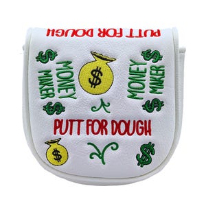 May include: White golf club head cover with the text "PUTT FOR DOUGH" in red. The cover features green dollar signs and the words "MONEY MAKER" in green. A yellow money bag with a dollar sign is in the center.