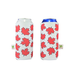 May include: Two white neoprene can coolers featuring a red maple leaf pattern. The coolers are designed to keep drinks cold.