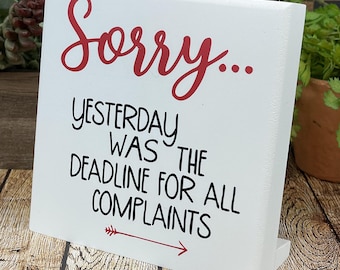 May include: A white wooden sign with the words "Sorry... Yesterday was the deadline for all complaints" in red and black lettering. A red arrow points to the right.