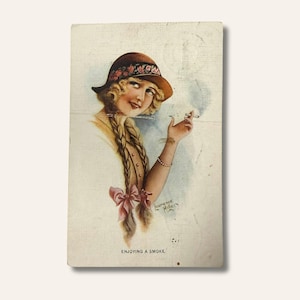 May include: Vintage postcard illustration of a woman with blonde braids, wearing a brown hat with a floral band, smoking a cigarette. The text "ENJOYING A SMOKE" is at the bottom. Signed "Lawrence Miller".