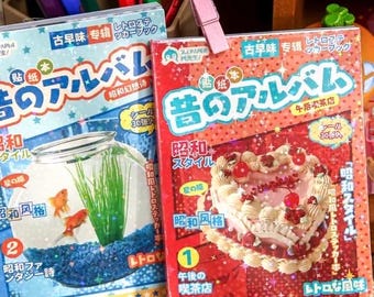 May include: Two Japanese sticker books with retro designs. One features a fishbowl with goldfish, the other a heart-shaped cake. Both have Japanese text and are in a box with a pink clip.