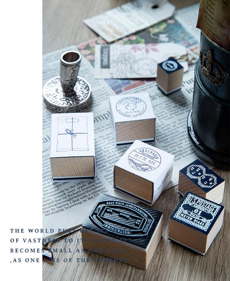 May include: A collection of vintage postage stamps and a silver ink stamp holder are arranged on a newspaper. The stamps feature various designs, including postal markings and text. The wooden bases and detailed designs create a nostalgic aesthetic.